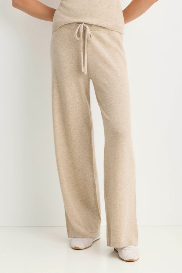 A person wearing light beige wide-leg knit pants with a drawstring waist, paired with a matching top and white shoes, shown against a plain white studio background.