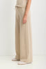 A person wearing loose, wide-leg knit pants in a light warm beige or oatmeal tone, paired with a matching top and pale slip-on shoes, photographed against a plain light background.